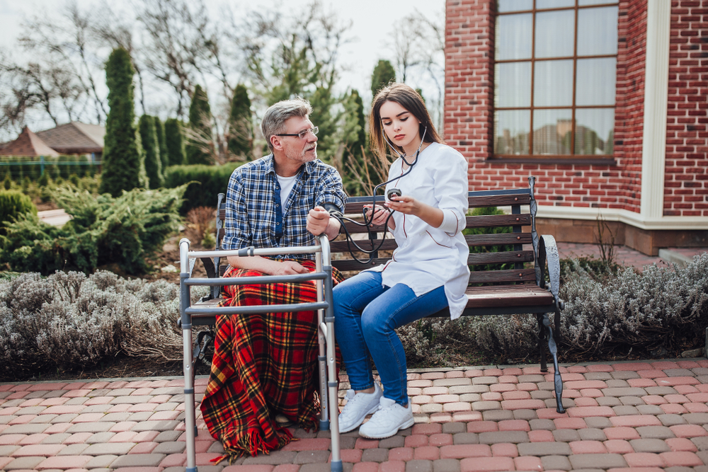 medical woman speaking with veteran on bench outside doing vital signs